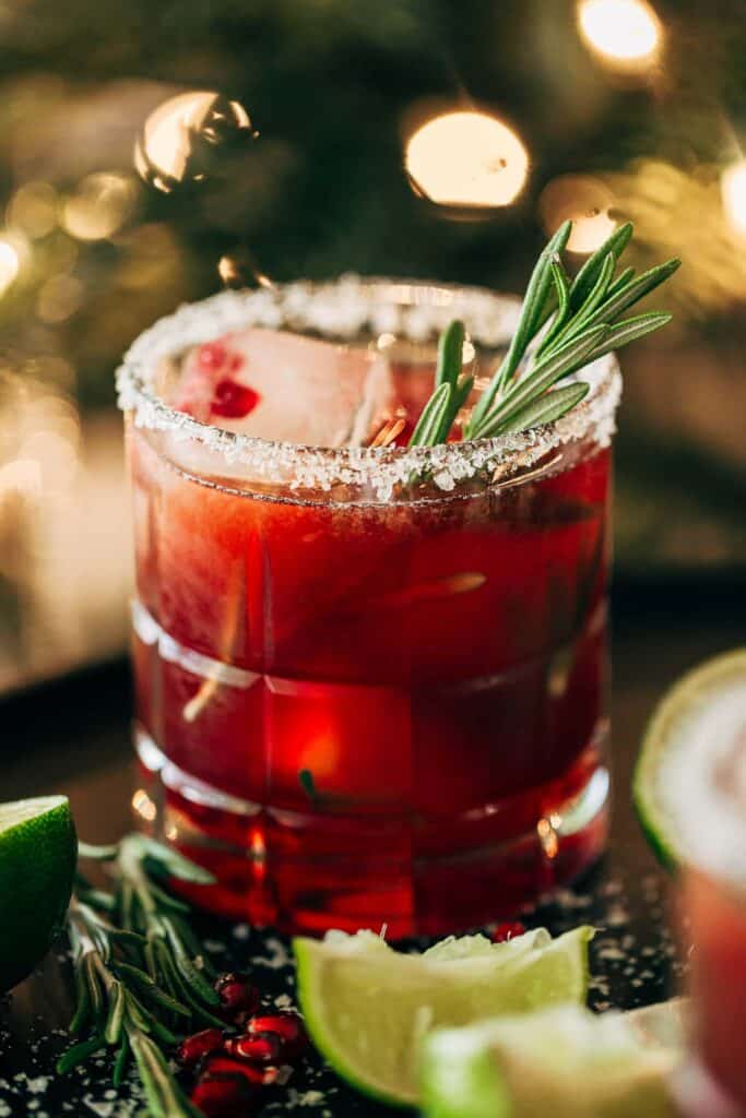 a pomegranate margarita with a salt rim and rosemary sprig