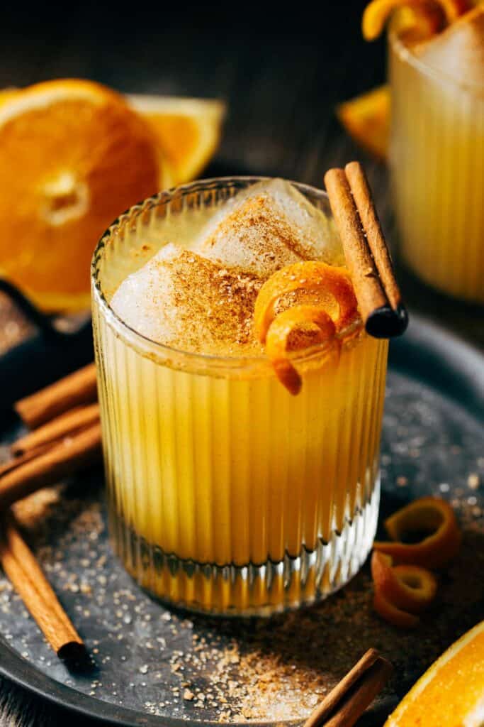 close up on an orange cocktail garnished with a cinnamon stick