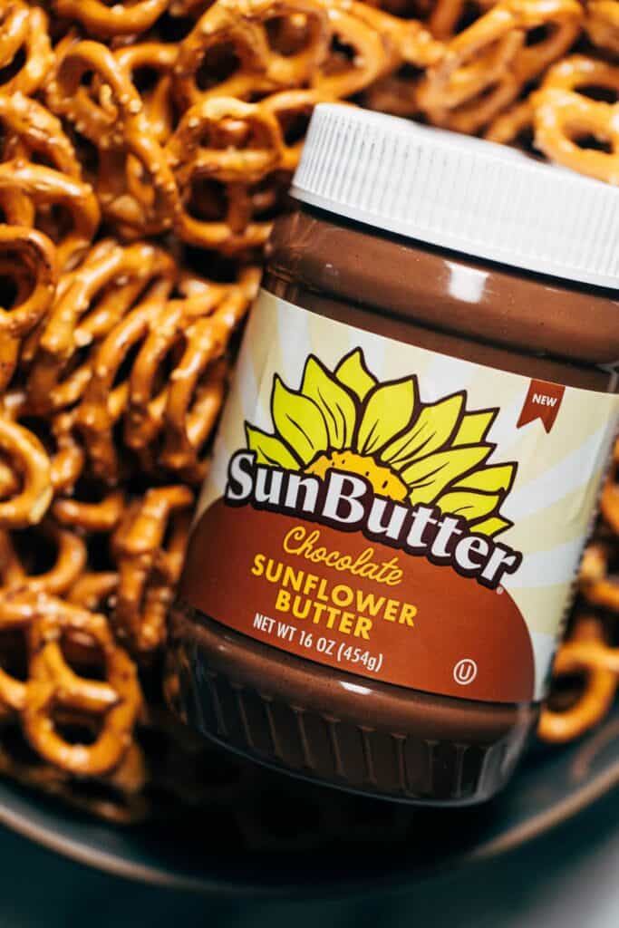 a jar of chocolate sunbutter in a bowl of pretzels