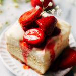 a strawberry shortcake cheesecake bar slice on a plate topped with strawberries