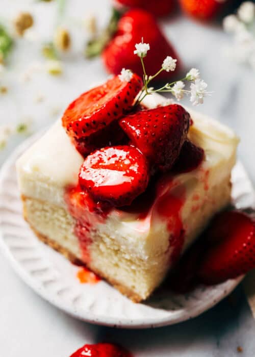 a strawberry shortcake cheesecake bar slice on a plate topped with strawberries