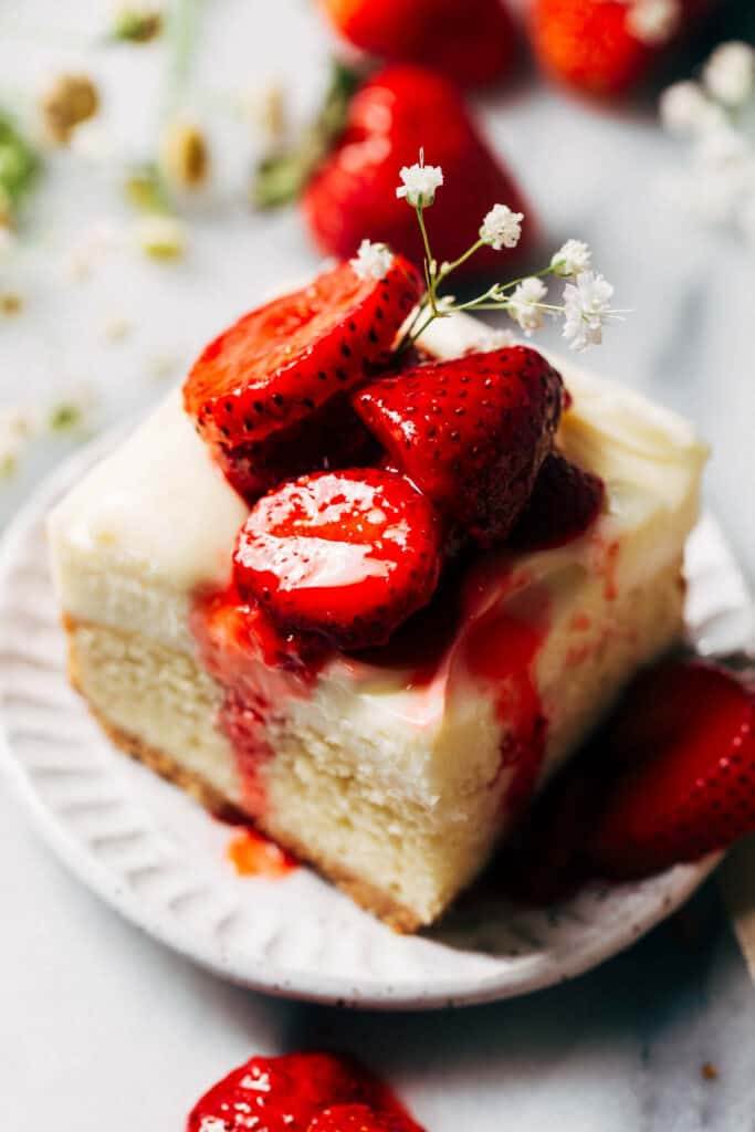 a strawberry shortcake cheesecake bar slice on a plate topped with strawberries