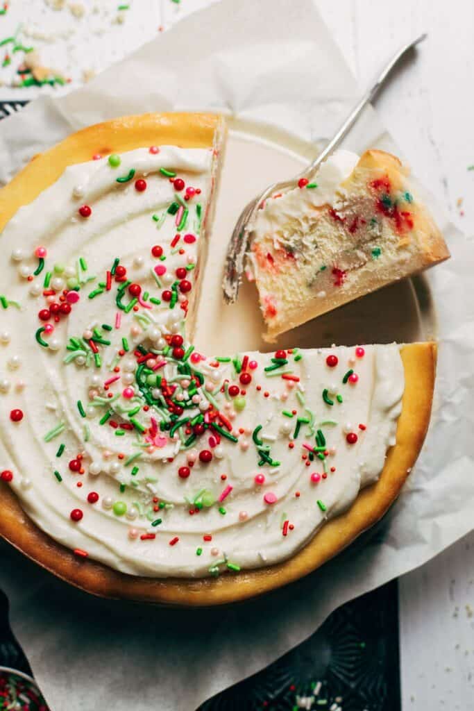 the top of a sliced sugar cookie cheesecake with frosting and sprinkles