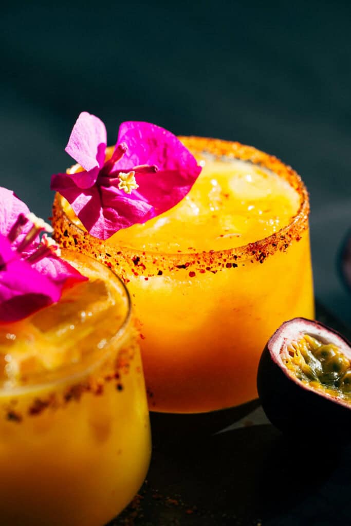 Close up on two spicy passion fruit margaritas accented by a sliced half of passion fruit