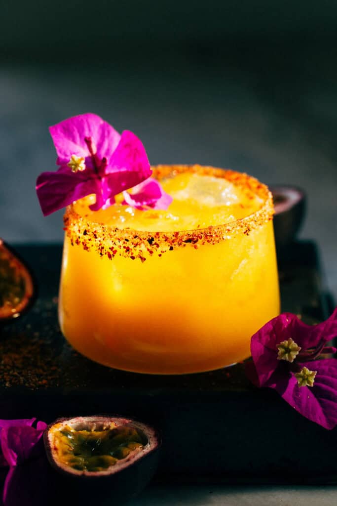 passion fruit margarita in a cocktail glass with a tajin rim and a decorate, edible flower