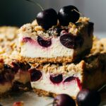 Close up of stacked cherry cheesecake bars with two cherries on top