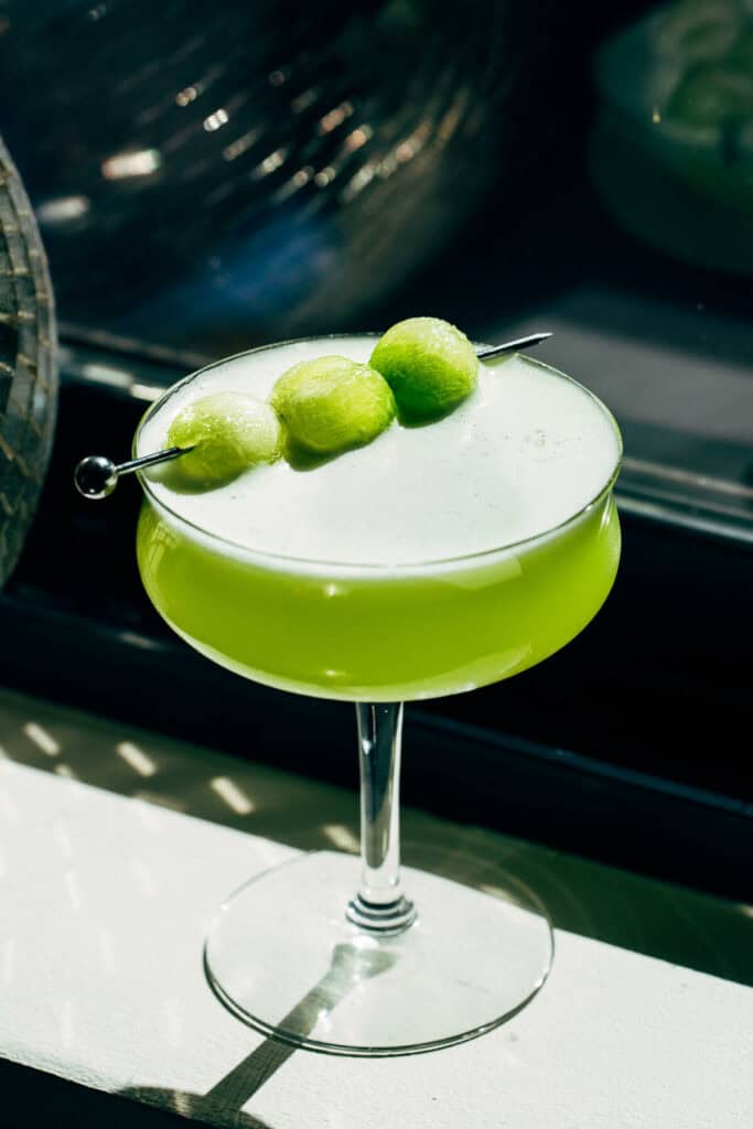 honeydew tequila sour in a coupe glass with melon ball garnish