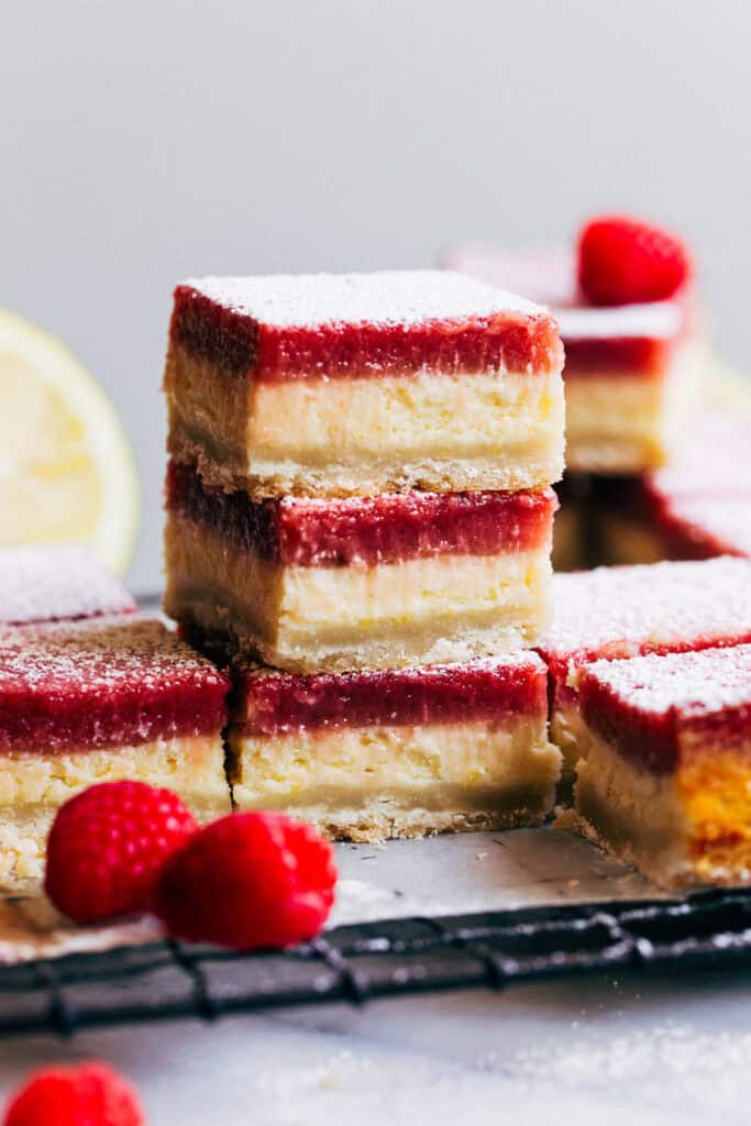 close up on stacked raspberry lemon cheesecake bars with two decorative raspberries by the stack