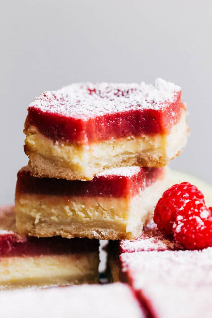 close up on raspberry lemon cheesecake bar with a bite taken out stacked on top of another cheesecake bar