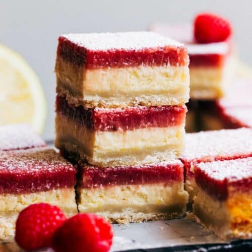 close up on stacked raspberry lemon cheesecake bars with two decorative raspberries by the stack