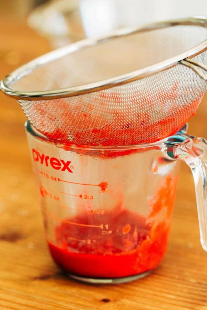 process shot of raspberry reduction being strained into a glass measuring cup