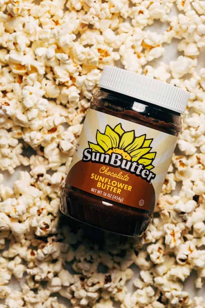 jar of sunbutter place on top of a layer of plain popcorn