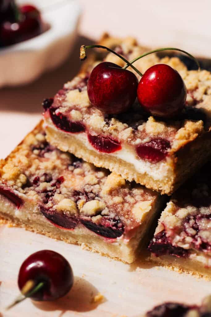 a stack of cheesecake bars baked with a layer of fresh cherries