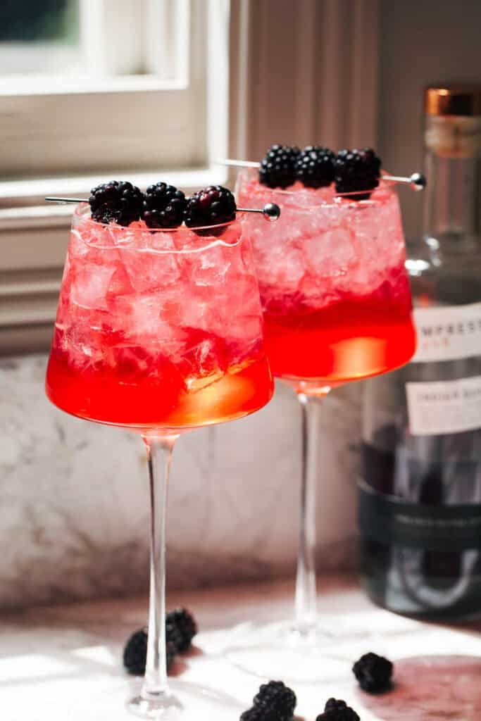 two blackberry gin spritzes in long-stemmed wine glasses