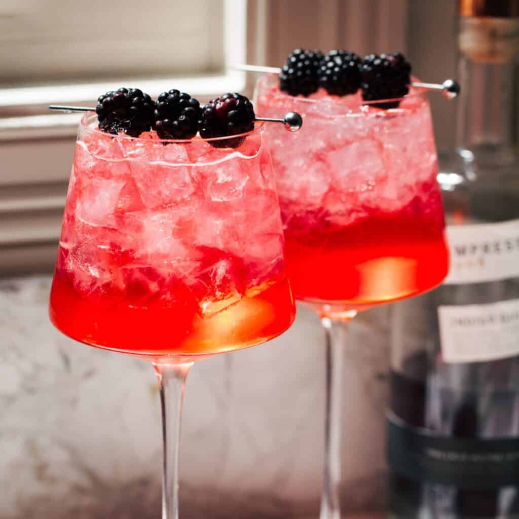 two blackberry gin spritzes in long-stemmed wine glasses